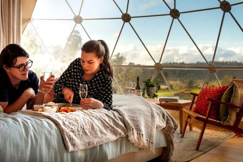 Ein Mann und eine Frau sitzen mit einer Mahlzeit auf einem Bett. in der Unterkunft Incredible Dome Getaway on a Vineyard Perfect for Glamping, Tasmania in Sidmouth
