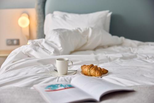 a cup of coffee and a croissant on a bed at Van der Valk Hotel Paris CDG Airport in Roissy-en-France