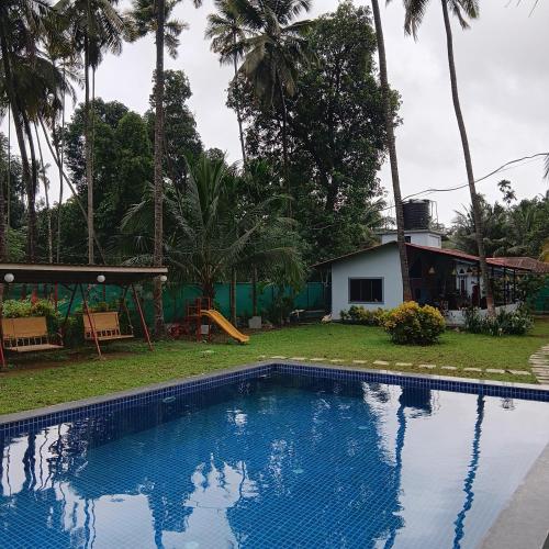 a swimming pool in front of a house with palm trees at Disha Villa in Alibag
