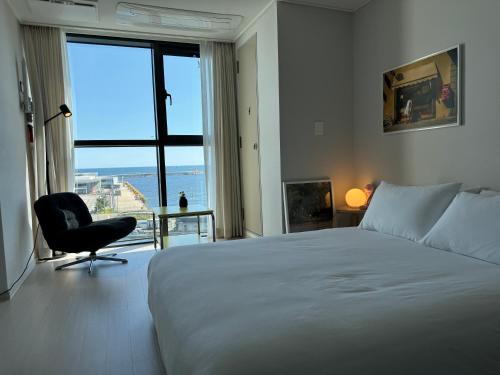 a bedroom with a bed and a chair and a window at 속초씨에 머물다, sokchosea in xiella in Sokcho