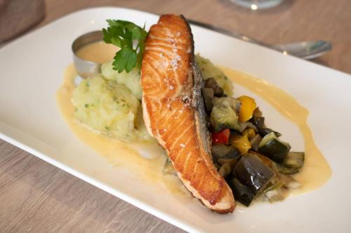 a white plate with a piece of fish with potatoes and vegetables at Brit Hotel Angers Parc Expo - L'Acropole in Saint-Sylvain-dʼAnjou