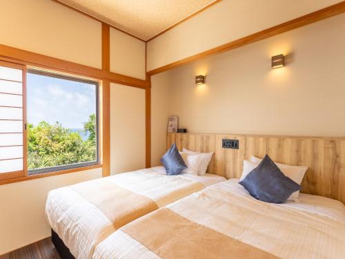 two beds in a room with a window at Livemax Resort Inami Seafront in Inami