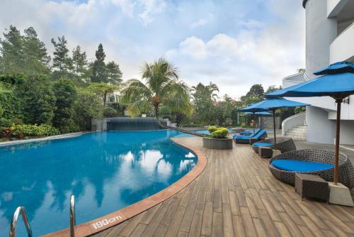 a swimming pool with chairs and umbrellas next to a building at ARTOTEL Suites Aquila - Bandung in Bandung