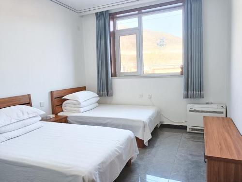 two beds in a room with a window at Jinshanling Great Wall聚友缘民宿 in Gubeikou