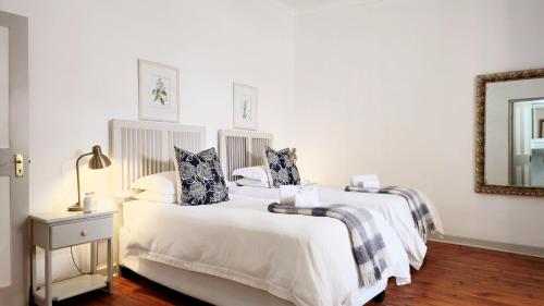 two beds in a white bedroom with a mirror at River Bend Guesthouses in Graaff-Reinet