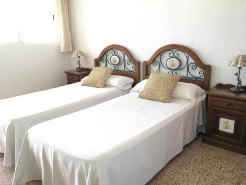 two beds in a room with white sheets at Apartamentos Bahia in Benidorm