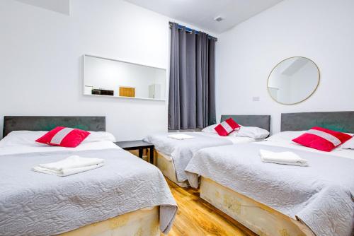a bedroom with two beds with red pillows and a mirror at Abbey Hotel in London