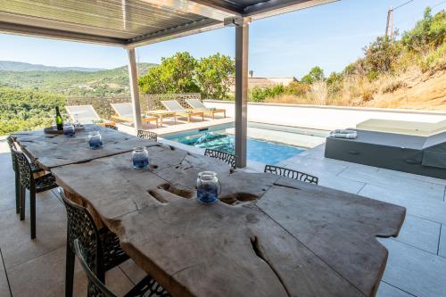 une grande table en bois sur un patio avec une piscine dans l'établissement NOUVEAU ! Maison de standing avec piscine et climatisation entre mer et montagnes, à Albitreccia