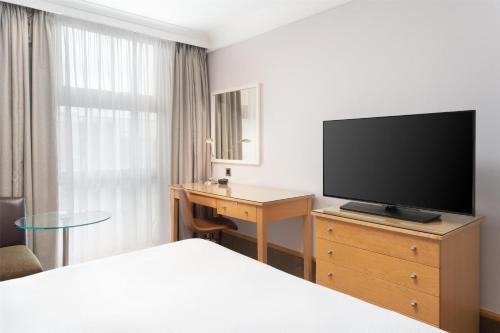 a hotel room with a bed and a television on a dresser at Hilton London Kensington Hotel in London