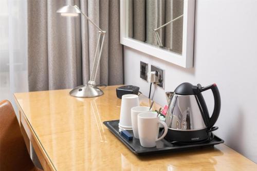 a coffee maker and cups on a wooden table at Hilton London Kensington Hotel in London
