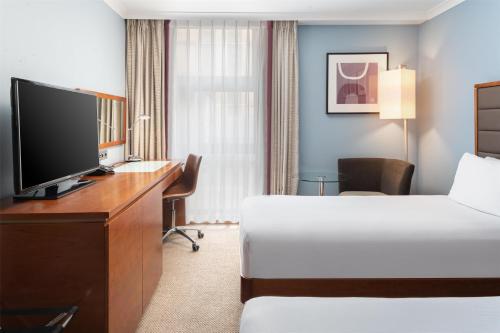 a hotel room with a bed and a desk with a television at Hilton London Kensington Hotel in London