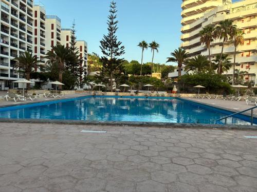 a large swimming pool with chairs and trees and buildings at Apartamento céntrico en Playa de Las Américas in Costa de Adeje