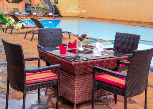a table with four chairs and a swimming pool at Lowlands Hotel & Spa in Chuka
