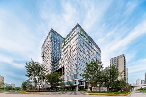 a tall glass building with trees in front of it at Holiday Inn Express Taizhou Jiaojiang in Taizhou
