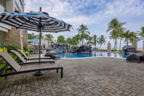 a pool with an umbrella and chairs next to a swimming pool at Diamante del Sol 303S- 3rd Floor Ocean View in Jacó