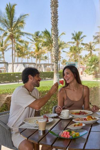 a man and woman sitting at a table with food at Salalah Rotana Resort in Salalah