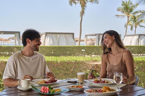 a man and woman sitting at a table with plates of food at Salalah Rotana Resort in Salalah