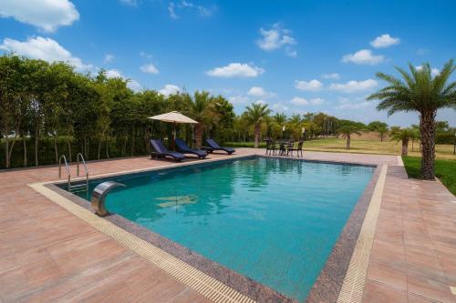 a swimming pool with chairs and a table and trees at Tata Vista Resort, Vrindavan - #big swimming pool #luxury rooms #gardens #playing zone #away from city hustle # BY ELEGANCE GROUP# in Vrindāvan