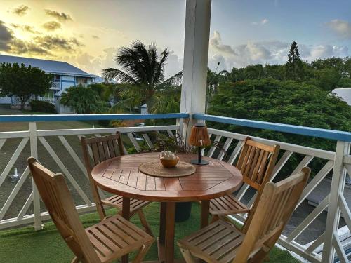 a wooden table on a porch with chairs and a lamp at Archipel Guadeloupéen - Entre grand balcon, piscine & lagon - Élégant cocon d'architecte 2 étoiles in Saint-François