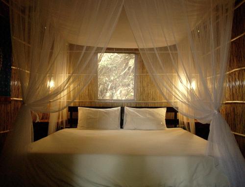 Gala Gala Eco Resort في بونتا دو أورو: غرفة نوم بسرير ابيض مع نافذة