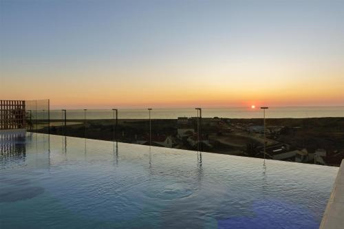 a swimming pool with the sunset in the background at Amarello Hotel Praia Santo André, Tapestry Collection by Hilton in Santiago do Cacém