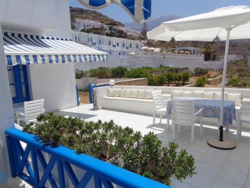 a patio with white chairs and a table and an umbrella at Blue and White Studios & Apartments in Lefkos Karpathou