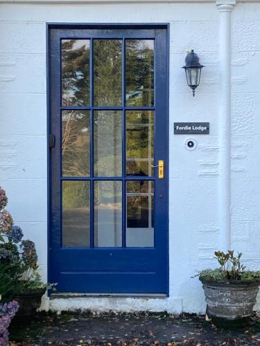 a blue door on a white house with a lamp at Fordie Lodge in Comrie