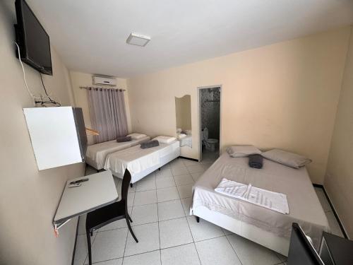 a room with two beds and a table and a tv at Pousada Casa Bela in Campina Grande