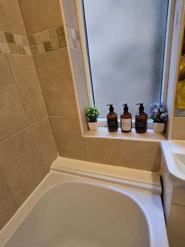 a bathroom with a bath tub and a window with three plants at 2bedroom Raynes Park London 30min to Central London Family Friendly in Raynes Park