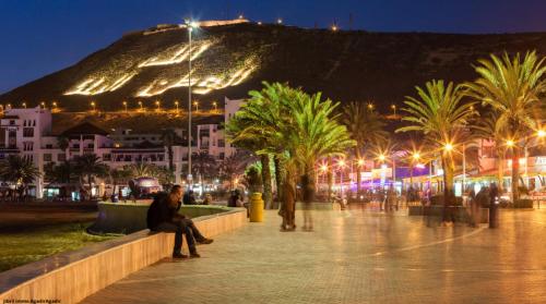 a man sitting on a bench at night with a mountain at L'adresse est près de la plage in Agadir
