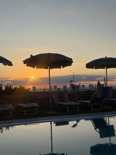 a pool with umbrellas and chairs with the sunset in the background at Hotel Villa Cimmentorosso in Ischia