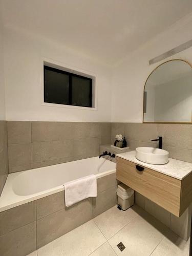 a bathroom with a tub and a sink and a mirror at Pantai Indah Cottage in Hervey Bay