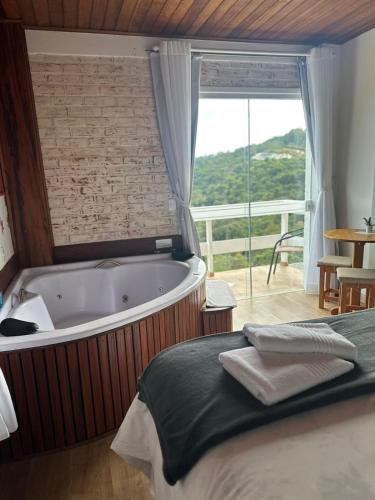 a bedroom with a tub and a bed and a window at Pousada Casa Pinha em Campos do Jordão in Campos do Jordão