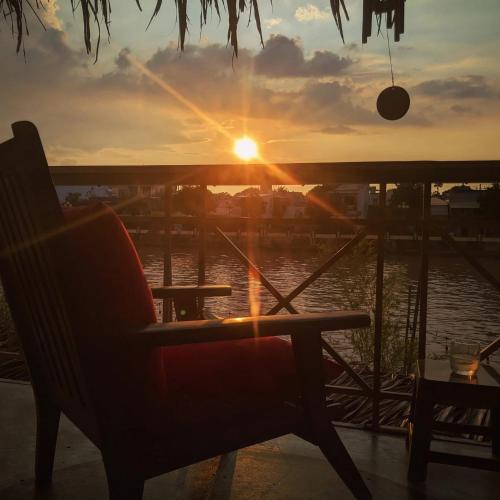 a chair on a porch with the sunset in the background at Here Library - A wooden home by the river with a library in Thốt Nốt
