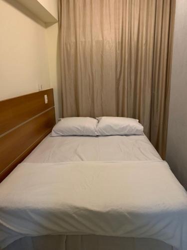 Una cama con sábanas blancas y almohadas en un dormitorio. en Flat Saint Moritz, en Brasilia