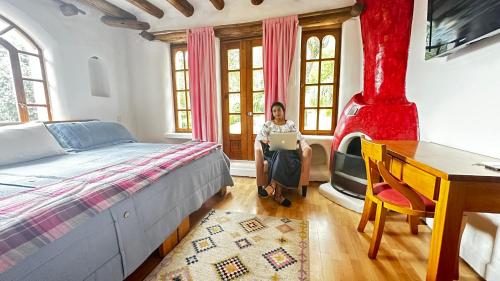 a woman sitting in a bedroom with a bed and a laptop at INTIYAYA - Boutique Lodge in Otavalo