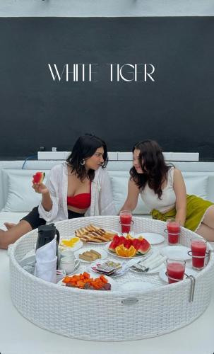 two women sitting on a bed with a table full of food at White Tiger Villa in Madgaon