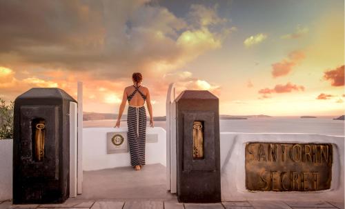 a woman standing in the doorway of a building with the sunset at Santorini Secret Suites & Spa, Small Luxury Hotels of the World in Oia