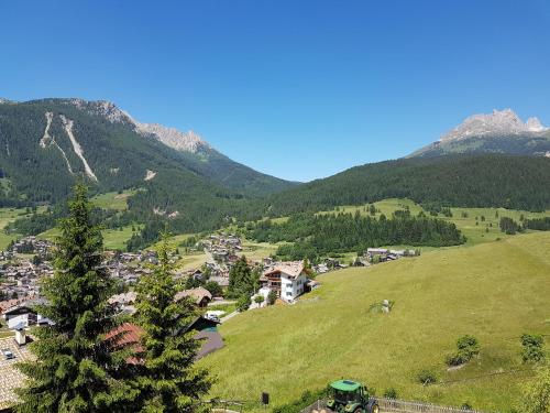 a village on a green hill with mountains in the background at Ciasa Alpina Relax Hotel in Moena