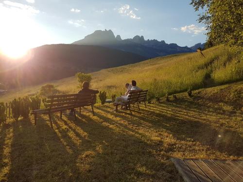 three people sitting on a park bench in a field at Ciasa Alpina Relax Hotel in Moena