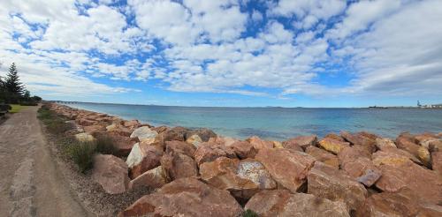 a rock wall next to the ocean with a cloudy sky at Esperance Ocean Escape in Esperance