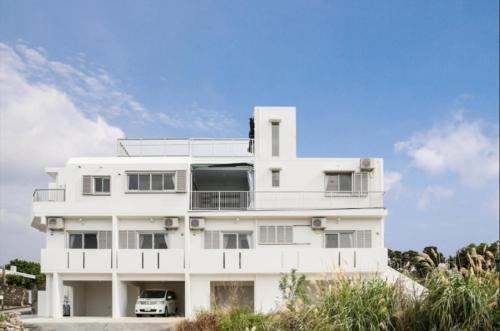 a white building with a car parked in front of it at Sun Set 海人 in Itoman