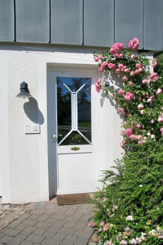 a white door with a window and pink flowers at Im-Pruemtal in Pronsfeld