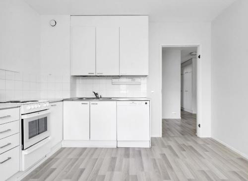 Cozy 2 Bedroom Apartment Near Santa Claus Village with space for 5 في روفانييمي: مطبخ أبيض مع دواليب بيضاء وأرضية خشبية