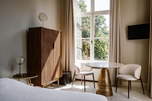 a bedroom with a bed and a table and a window at Hotel Kasteel Hoekelum in Bennekom