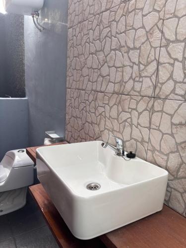 a white sink in a bathroom with a stone wall at Ekas Rising Coffee And Cottages in Ekas