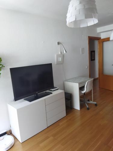 a living room with a tv on a white cabinet with a desk at El Mirador de la Estación in Canfranc-Estación