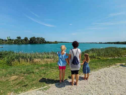 a woman and two girls standing on a path looking at a lake at Balajceva domačija - Moravske Toplice in Moravske Toplice