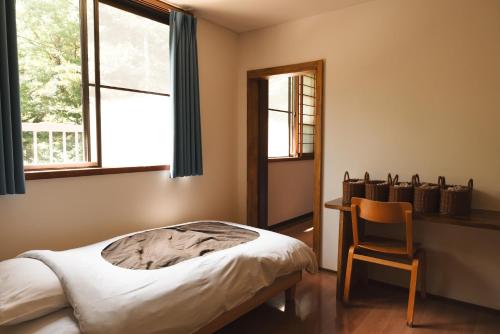 a bedroom with a bed and a chair and a window at Raicho Onsen Inn in Matsumoto