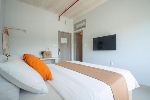 a bedroom with a white bed with an orange pillow at The Up Hotel Phu Quoc Island - The Poolside Escape in Phu Quoc